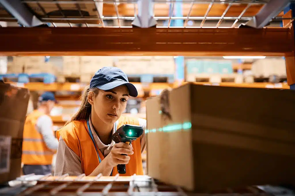 Warehouse associate scanning a carton on a shelf with a handheld barcode reader during pick and pack