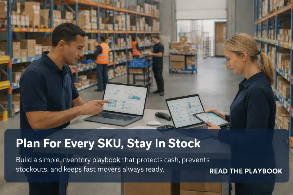 Two coworkers review SKU inventory charts on a laptop and tablet at a warehouse desk while workers pick products in the aisles.