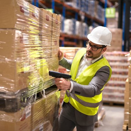 Working at warehouse. Male warehouse worker using bar code scanner to analyze newly arrived goods for further placement in storage department. Employee organizing goods distribution to the market.